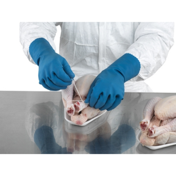 A person in a white coat and blue gloves cutting up a chicken in a kitchen.